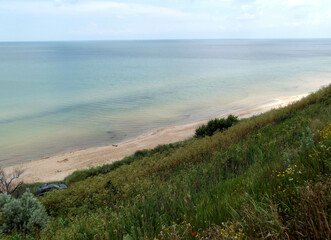 Azov sea coastal area with smooth green grass slope. Seashore view with sandy undeclared beach, blue sky horizon and a car.