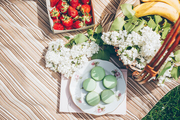 Overhead on summer picnic. Strawberries, macaroons, beverage and basket with flowers white lilac - 500852895