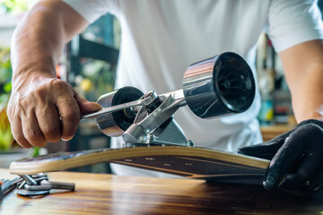 man use the socket tool to remove the nuts on skateboard and adjusts suspension in workshop,...