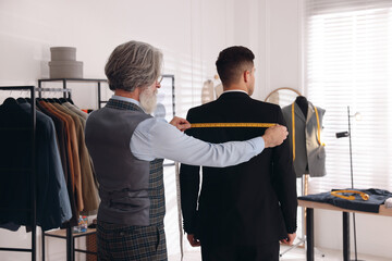 Professional tailor working with client in atelier, back view