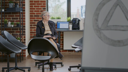 Psychologist sitting in circle with chairs and waiting on people at aa group meeting. Woman...