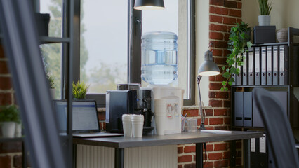 Close up of water dispenser and coffee machine on table for people working in office. Water cooler on desk with cups and equipment used for liquid refreshment and beverage on break. - Powered by Adobe