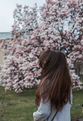 Brunette young woman is standing near a beautiful big pink magnolia tree