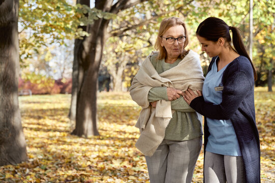 Senior woman talking with nurse walking at public park