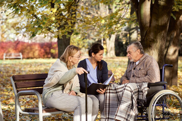 Caretaker discussing documents with disabled man and senior woman at park
