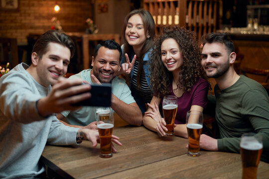 Group of happy friends having beer and taking a selfie in a pub