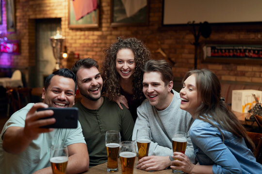 Group of happy friends having beer and taking a selfie in a pub