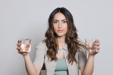 Beautiful woman holding glasses of water against gray background