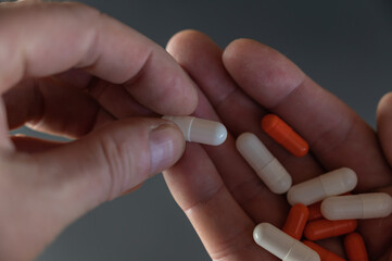 A man is holding white and orange medicine pills. The medicine lies in the open palm of an adult's hand. Health and Medicine.
