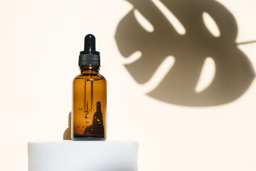 Women's cosmetic product in an amber bottle with a skin care pipette on the podium, background and shadow from the palm. copy space