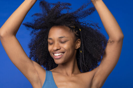 Smiling young woman with eyes closed dancing against blue background