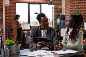 Executive managers analyzing marketing statistics using tablet computer working at company project during business meeting in startup office. Diverse team brainstorming ideas planning strategy