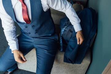 A young businessman in a blue suit takes the suit in his hand and puts it on