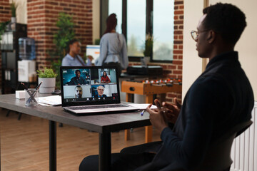 Marketing agency office worker talking with coworkers on digital video meeting call while in office. Company employee on remote videocall conference with clients talking about project revenues