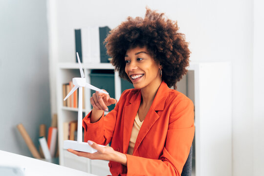 Smiling businesswoman with windmill model sitting in office