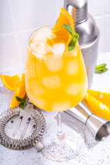 Orange and mint alcohol cocktail, aperol spritz, mimosa drink in long cocktail glass, with fresh orange slice garnish, white tiled background with bar utensils, copy space