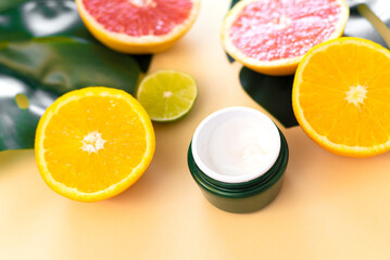 Jar of face moisturizer with natural citrus essential oil and orange and lime fruit background. Skin care cosmetic product mockup. Cosmetics with vitamin c