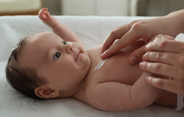 Mother applying body cream on her little baby indoors