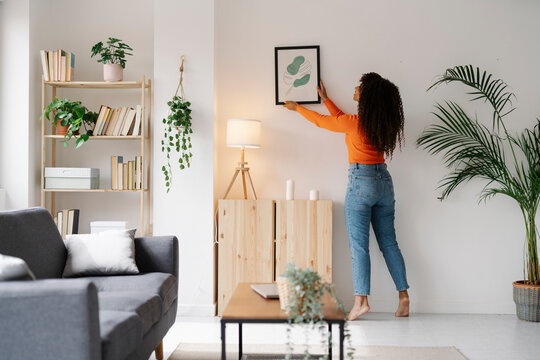 Young woman hanging picture frame on wall in living room at home