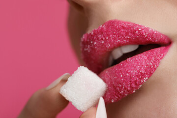 Closeup view of young woman with beautiful lips holding sugar cube on pink background