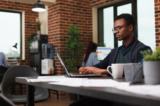 Advertisement company employee working on project marketing strategy using work laptop. African american financial advisor processing accounting data numbers while in modern office interior. - Powered by Adobe