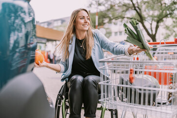Smiling woman with groceries sitting in wheelchair by shopping cart