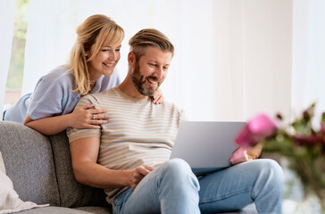 Obraz premium Happy couple sitting on couch at home and using laptop