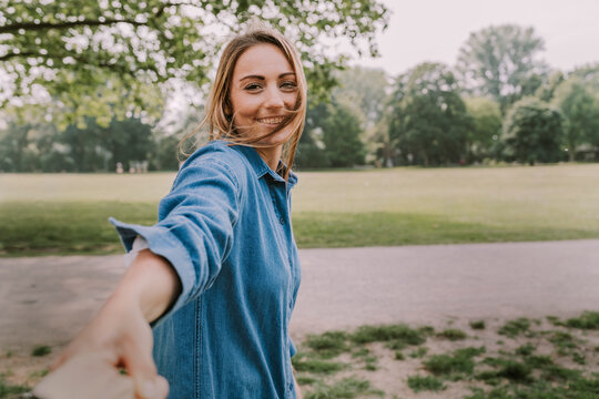 Smiling young woman pulling friend's hand in park