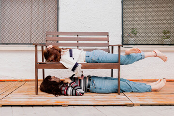 Woman lying on bench over friend at back yard