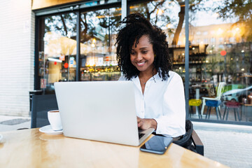 Happy businesswoman using laptop sitting at sidewalk cafe