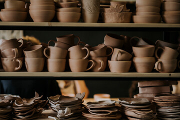 Handmade ceramic bowls with cups and plates on shelf in workshop