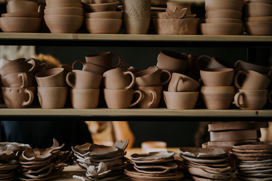 Handmade ceramic bowls with cups and plates on shelf in workshop