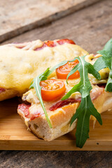 Appetizing homemade pizza on a baguette with cheese, tomatoes, arugula and sausages close-up.