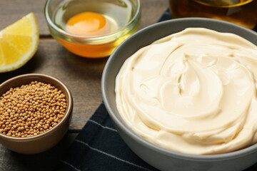 Bowl with fresh mayonnaise and ingredients on wooden table, closeup