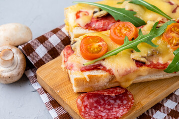 Pizza cooked on a baguette with cheese and sausages, pizza sandwich close-up, gray background.