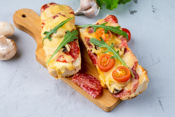 Two pieces of pizza cooked on a baguette, pizza sandwich on wooden boards, gray background.