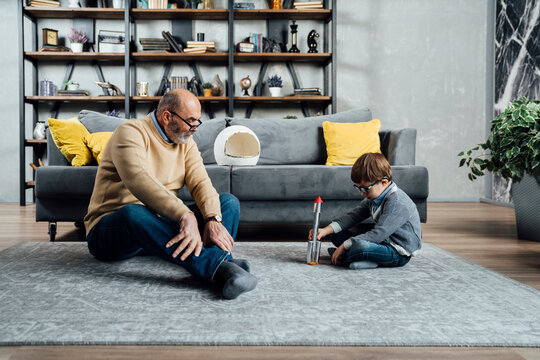 Grandfather looking at son playing with toy rocket in living room at home