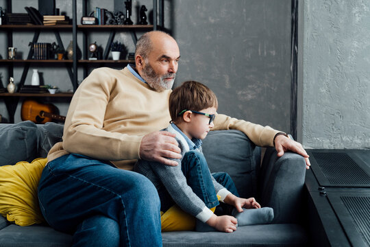 Senior man with grandson sitting on sofa in living room at home