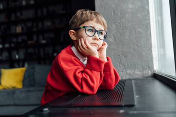 Boy wearing red sweater sitting with head in hands leaning on window sill