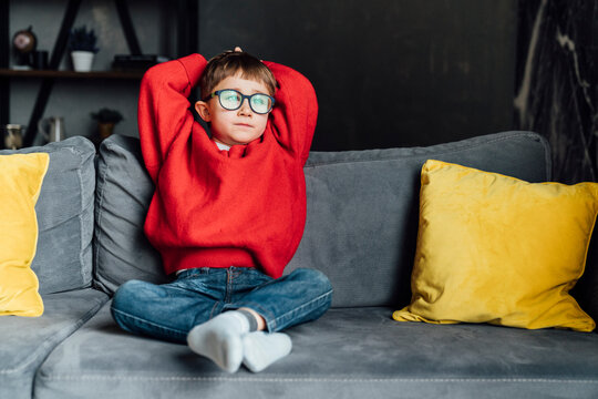 Cute boy sitting with hands behind head on sofa in living room