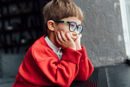 Cute boy wearing red sweater sitting with head in hands at home
