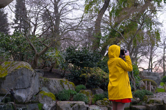 Woman wearing yellow raincoat photographing in forest