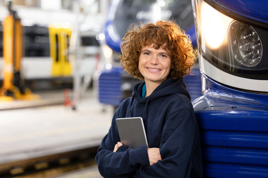 Smiling engineer holding tablet PC leaning on monorail in factory