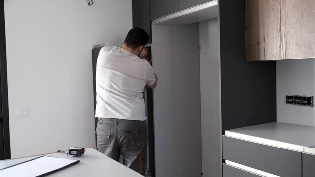 Young hispanic man installing furniture in the kitchen using a screwdriver. Assembling modern kitchen furniture.