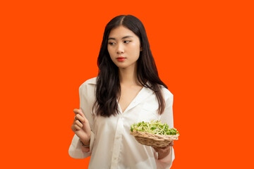 Vegetarian concept, Healthy woman hold basket of sunflower sprouts isolated over orange background