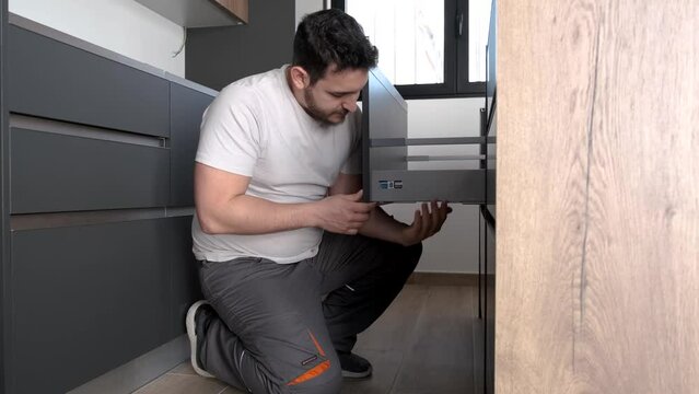 Young hispanic man adjusting a drawer height in a new modern kitchen. Assembling modern kitchen furniture.