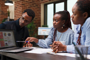Research agency employee pointing out financial data error on laptop screen. African american business people discussing about startup project method of development and future expenses.