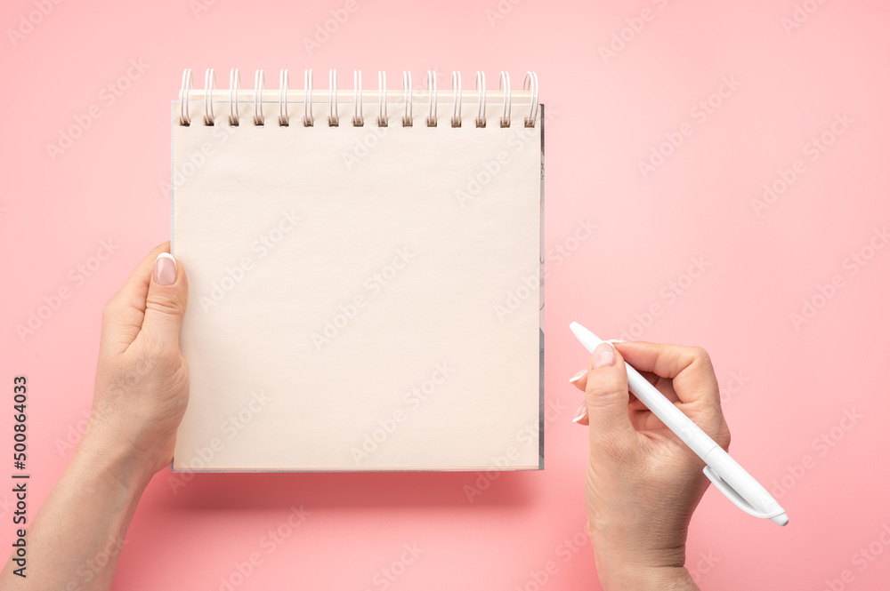 Aufkleber writing in blank notepad on pink background. female hands writing in mockup notepad. woman writing i