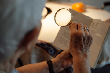 Senior woman with magnifying glass reading book at home