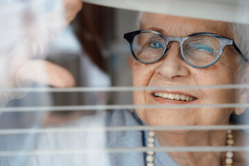 Happy senior woman looking through window blinds